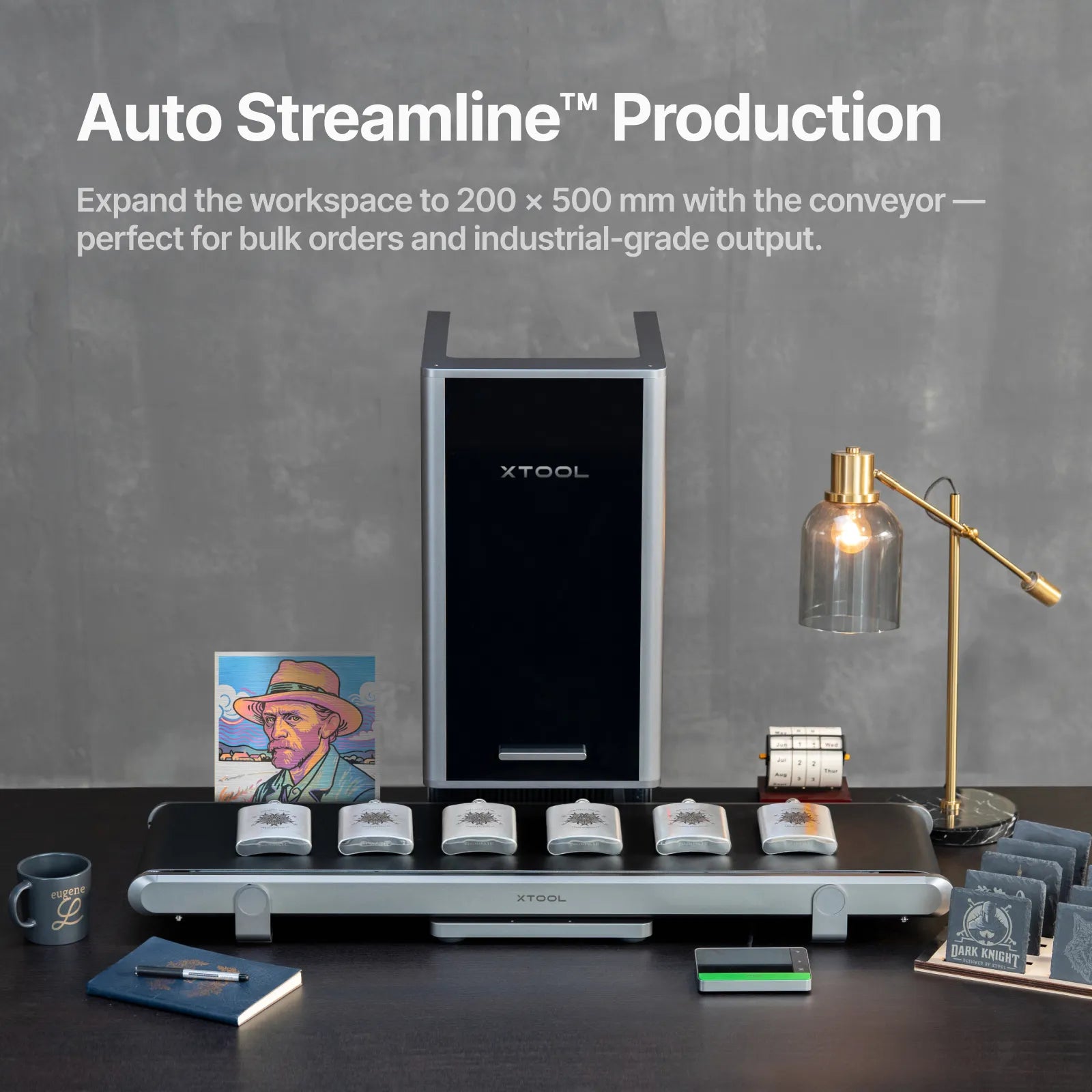 The front of the xTool F2 Ultra with the conveyor attached showing finished products including whiskey flasks, coasters, a mug, portrait and notebook.