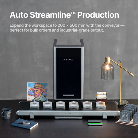 The front of the xTool F2 Ultra with the conveyor attached showing finished products including whiskey flasks, coasters, a mug, portrait and notebook.